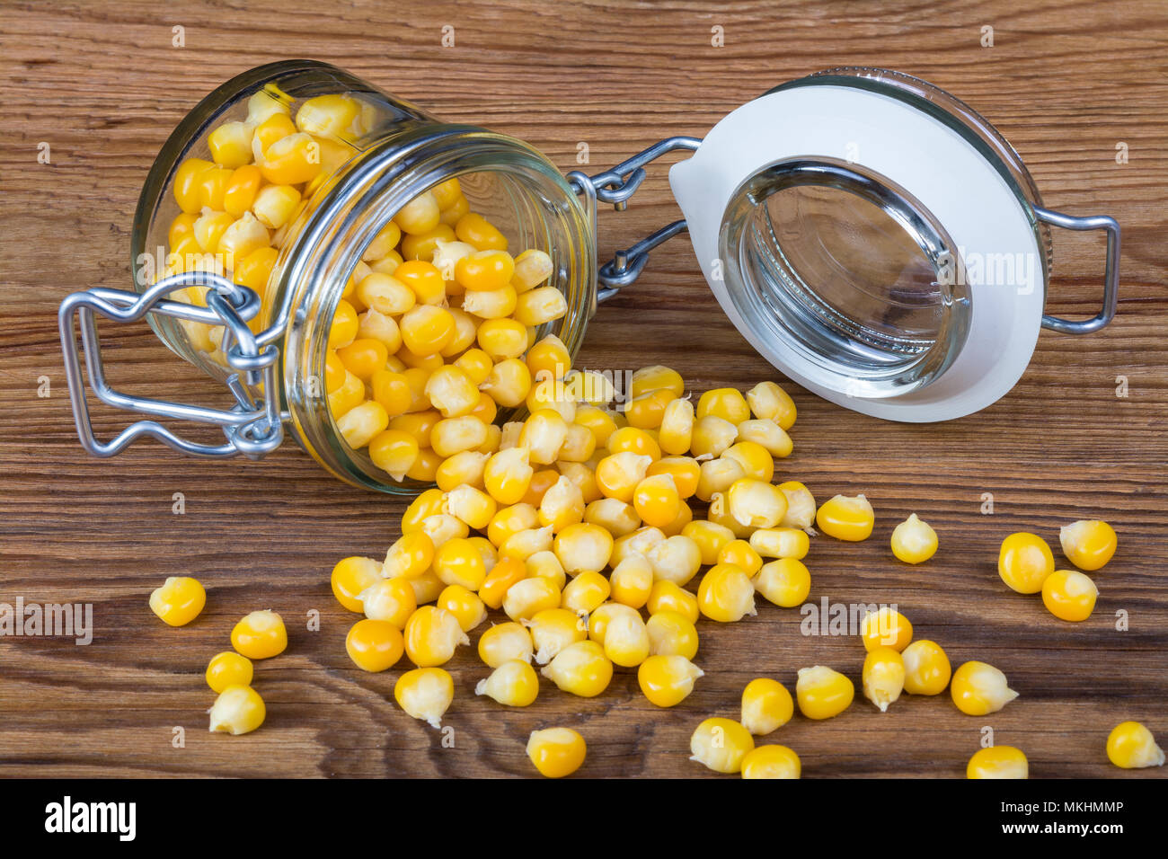 Boiled corn grains spilled on a wood background. Tasty and healthy vegetarian snack from yellow maize in a lying glass jar. Stock Photo