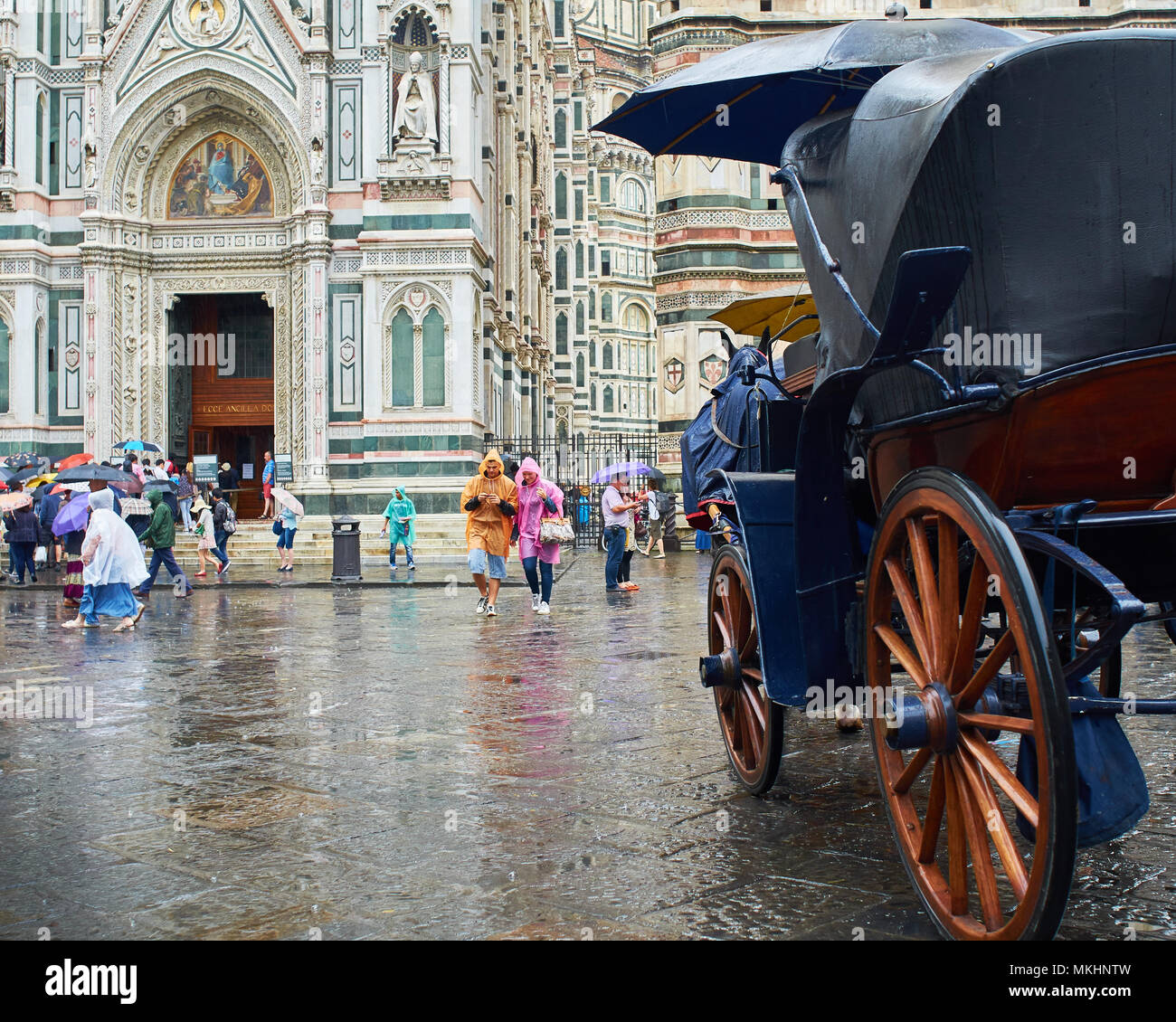 Tourists pass between the Duomo and a horse carriage during a rain ...