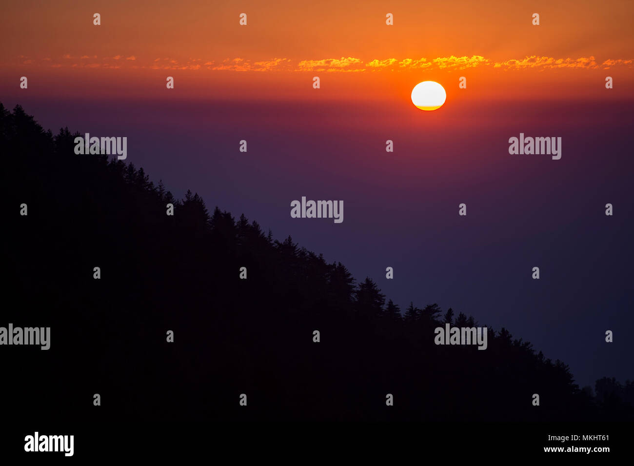 Amazing sunset behind a mountain with the silhouette of trees, Dharamsala, India. Stock Photo
