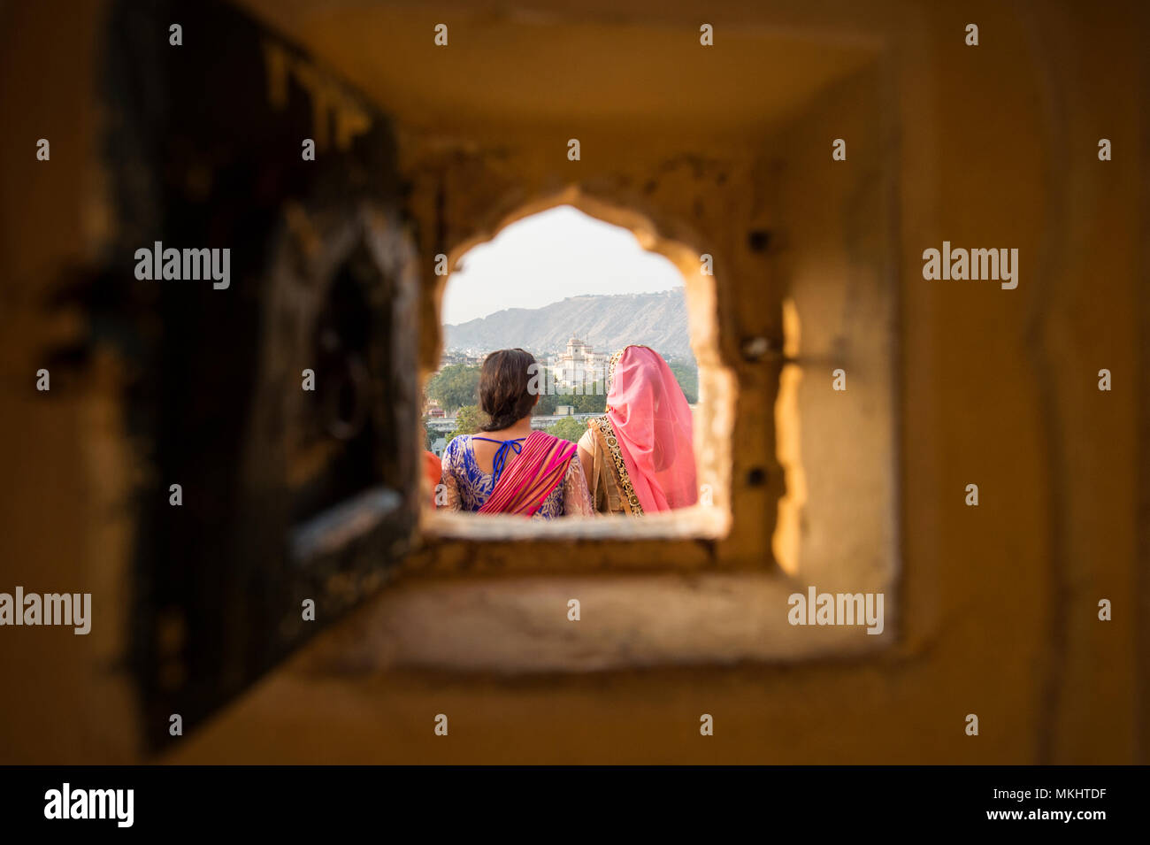 Two Indian girls wearing the traditional Indian dress 'Saree' are admiring the landscape of Jaipur. Photo taken from a small window on the Hawa Mahal  Stock Photo