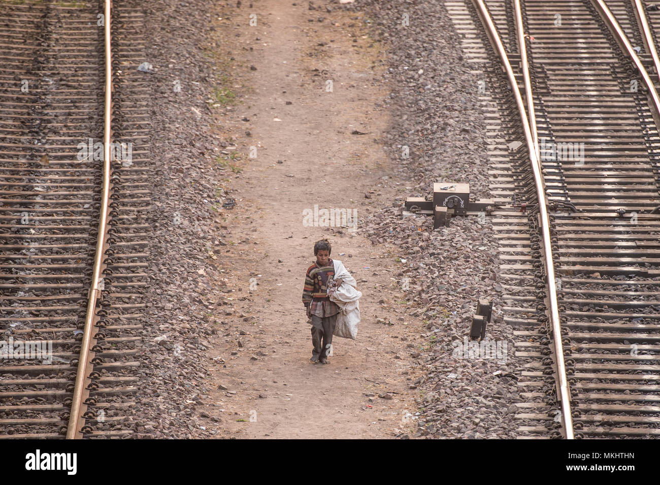 NEW DELHI - INDIA - 14 DECEMBER 2017. A poor child is walking through the railroads looking for something to eat and plastic bottles to recycle. Stock Photo