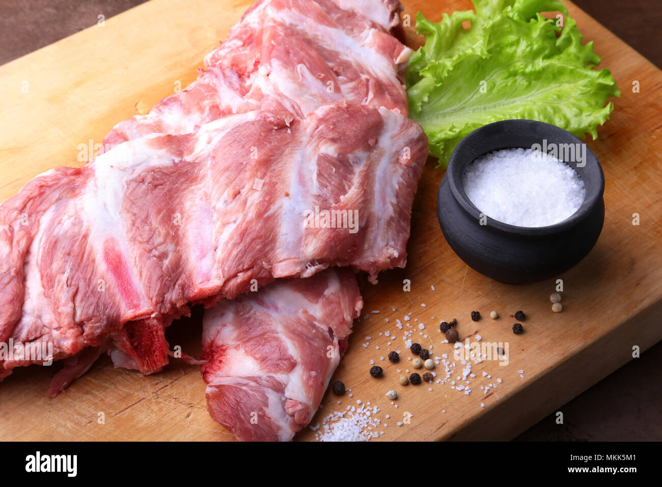 Raw Ribs on a rustic cutting board with salt, pepper and grinder for