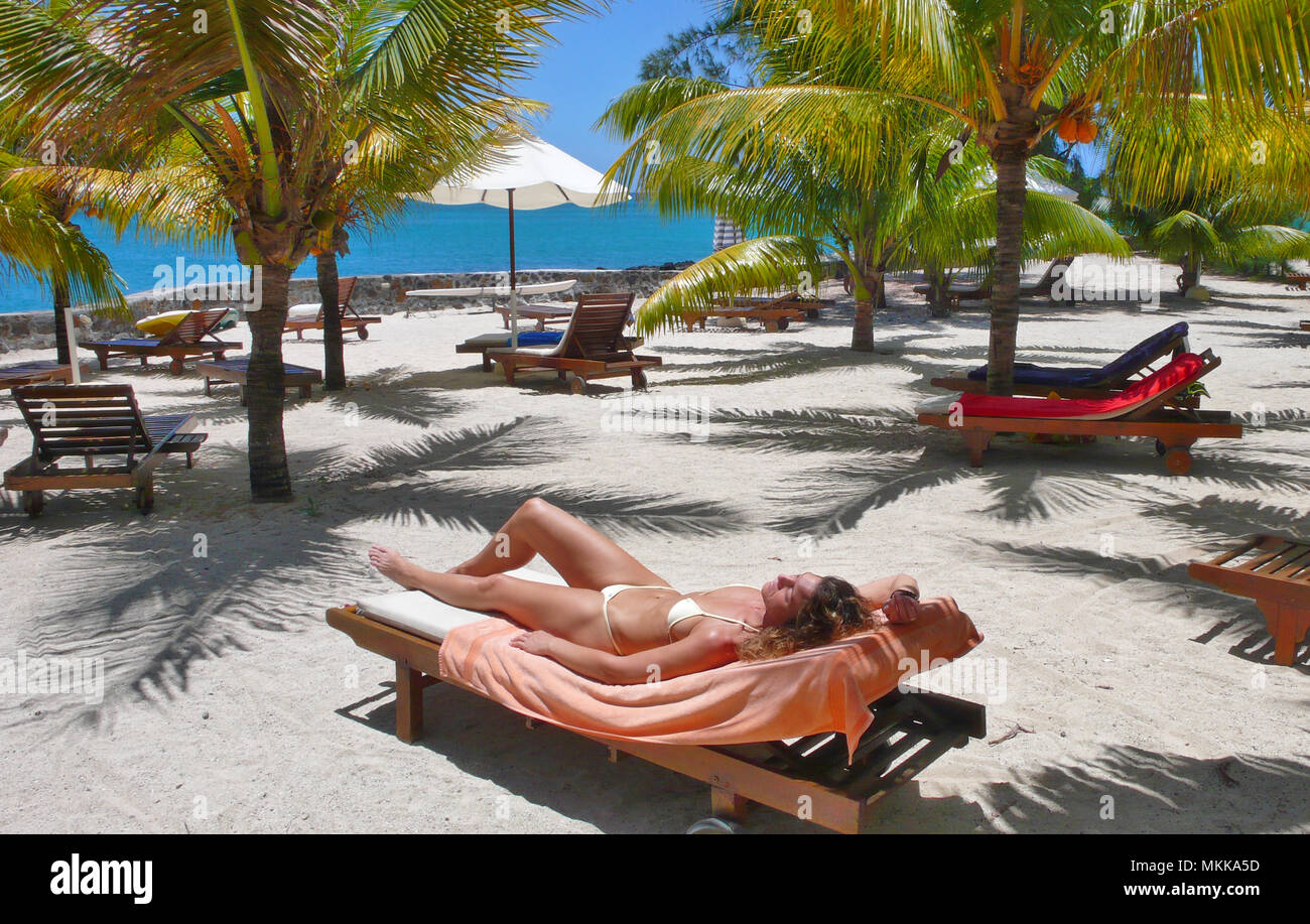 junge Frau sonnt sich unter Palmen am Meer | young woman sunbathing under palmtrees on a lounger at a sandy beach Stock Photo