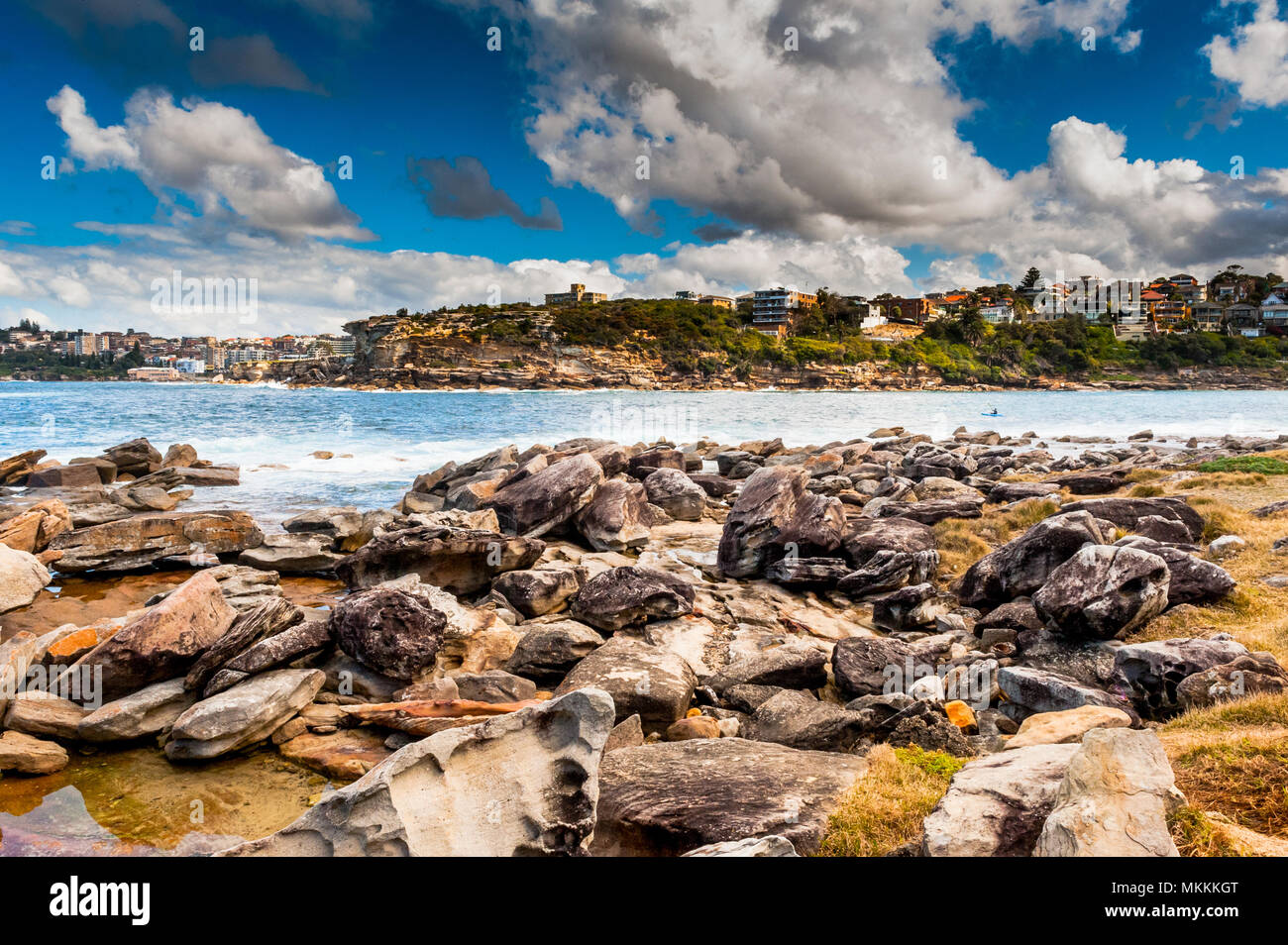 A single canoe makes its way across a bay between Bondi Beach and Coogee beach near a rocky shore line on a  beautiful day in Sydney Australia. Stock Photo