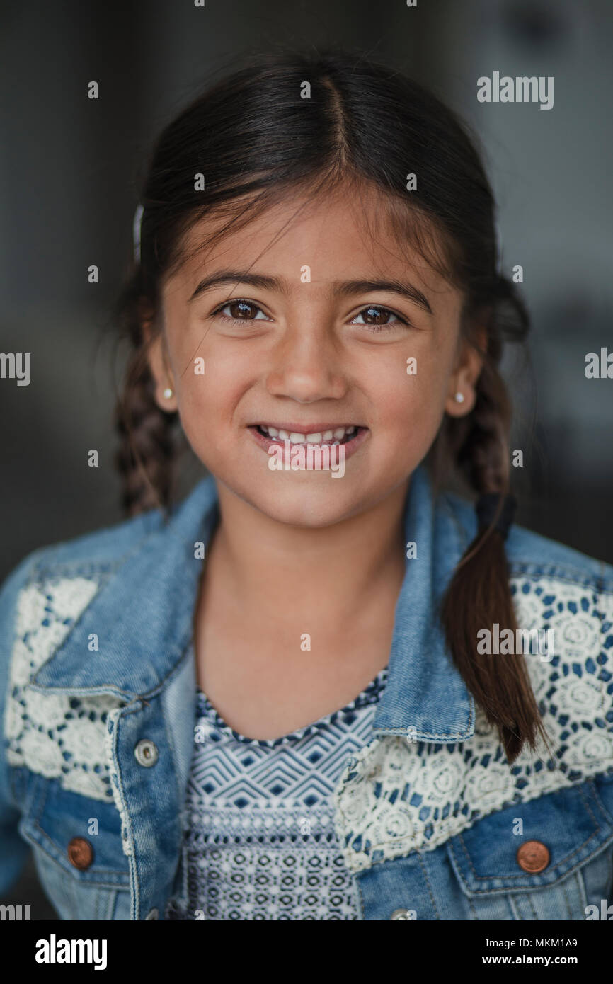 Portrait of a beautiful young girl smiling for the camera wearing a denim jacket with her hair in plaits. Stock Photo