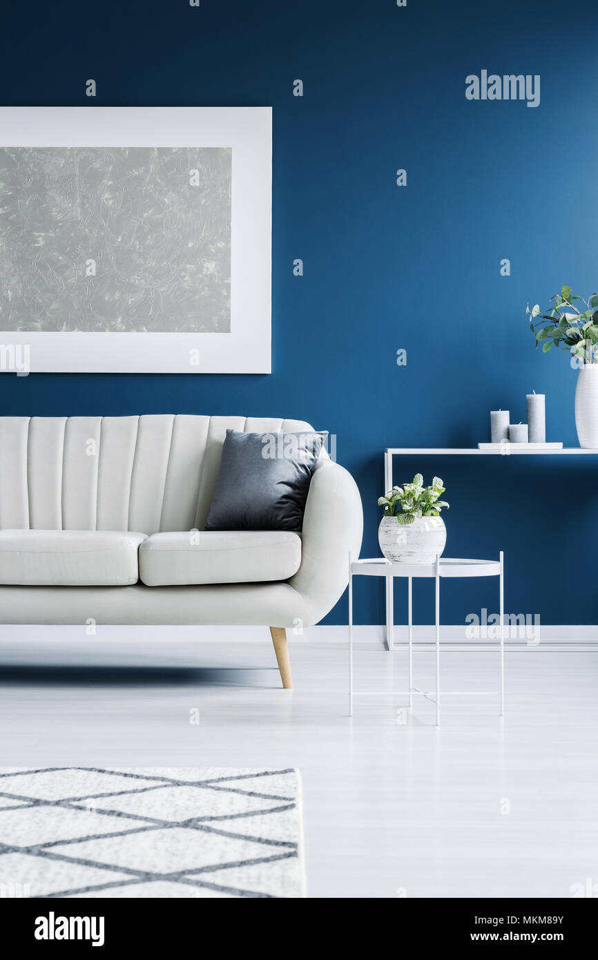 White, leather couch, tables, plants and big painting in a blue living room interior Stock Photo