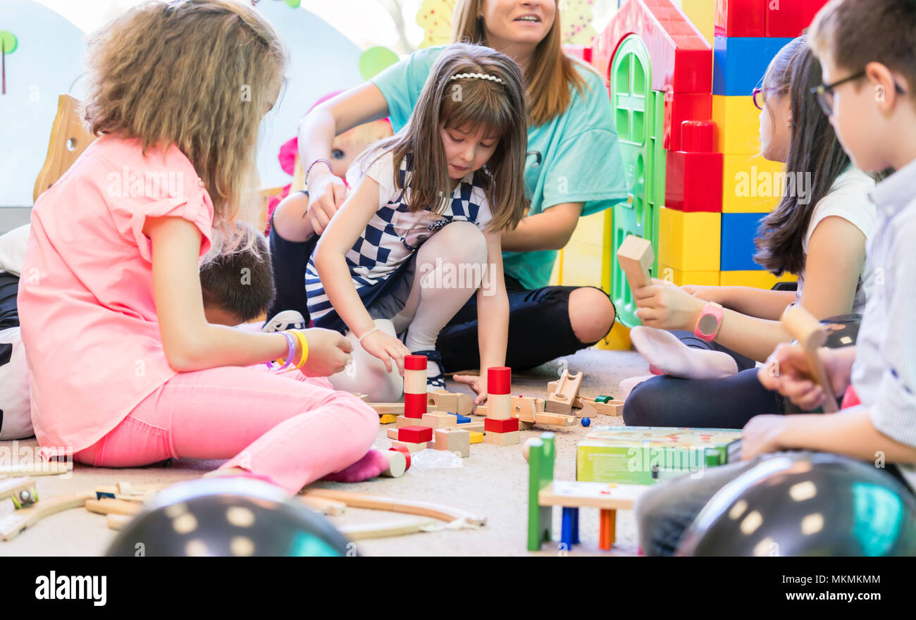 Dedicated kindergarten teacher holding a shy girl while watching children play Stock Photo