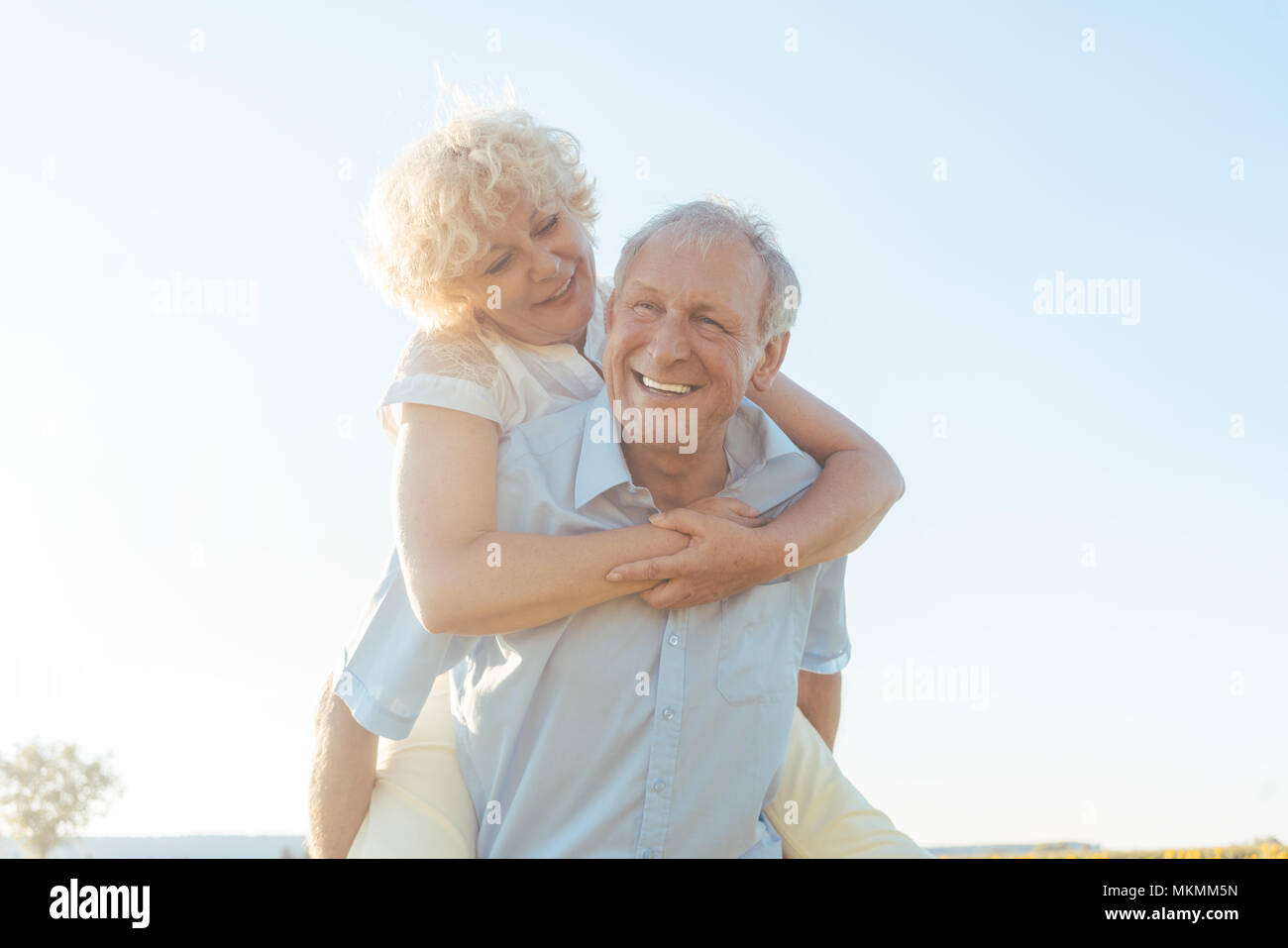 Happy senior man laughing while carrying his partner on his back Stock Photo
