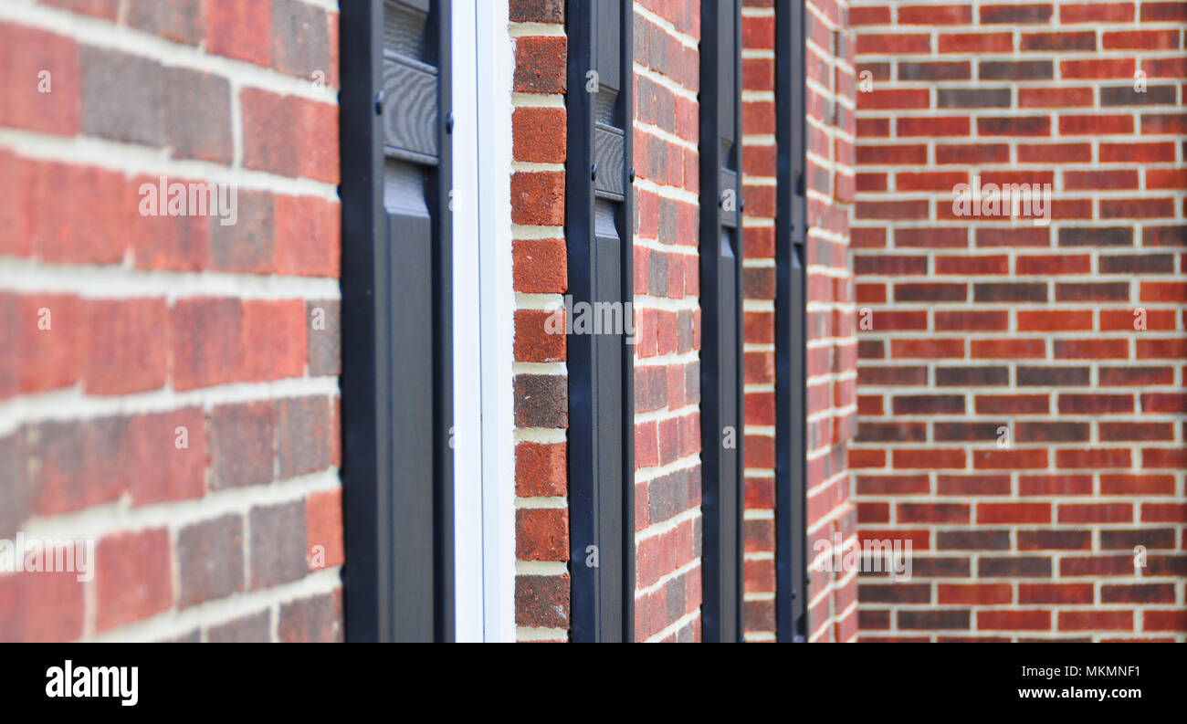 An abstract photograph of the exterior of a house. The photo has a shallow depth of field and shows exterior window trims and a red brick wall. Stock Photo