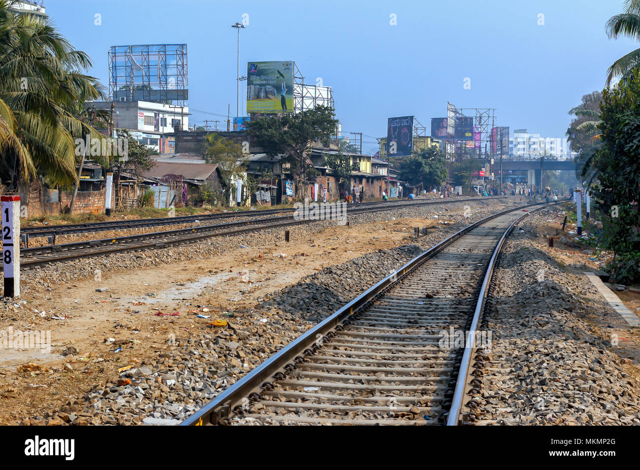 People walking nonchalantly on the sleepers of a railway tracks, in India. Residential houses and commercial establishments abuts the tracks. Stock Photo