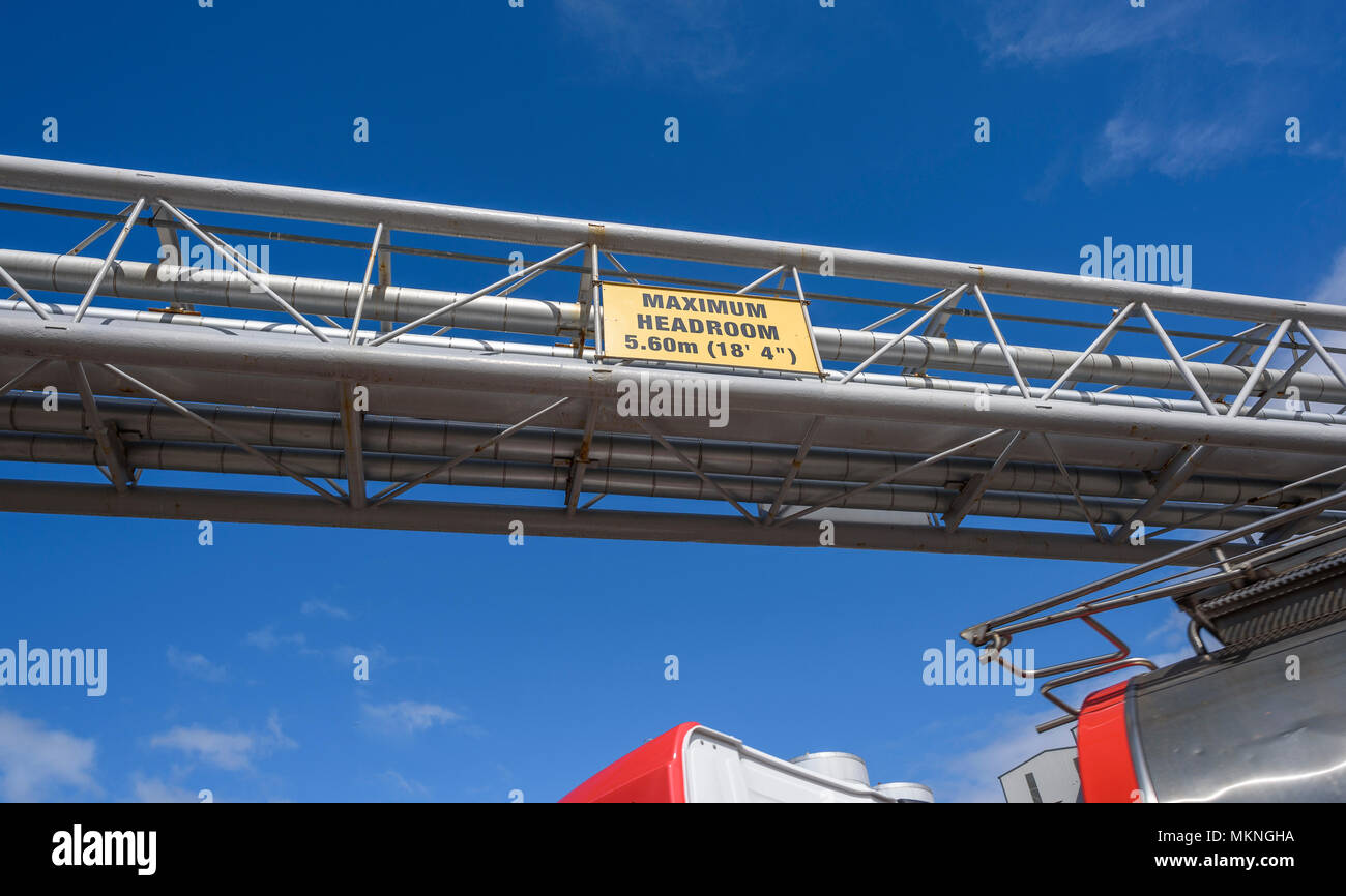 Headroom warning sign on an industrial plant for traffic allowing up to 5.60m (18'4') with passing HGV tanker underneath. Stock Photo