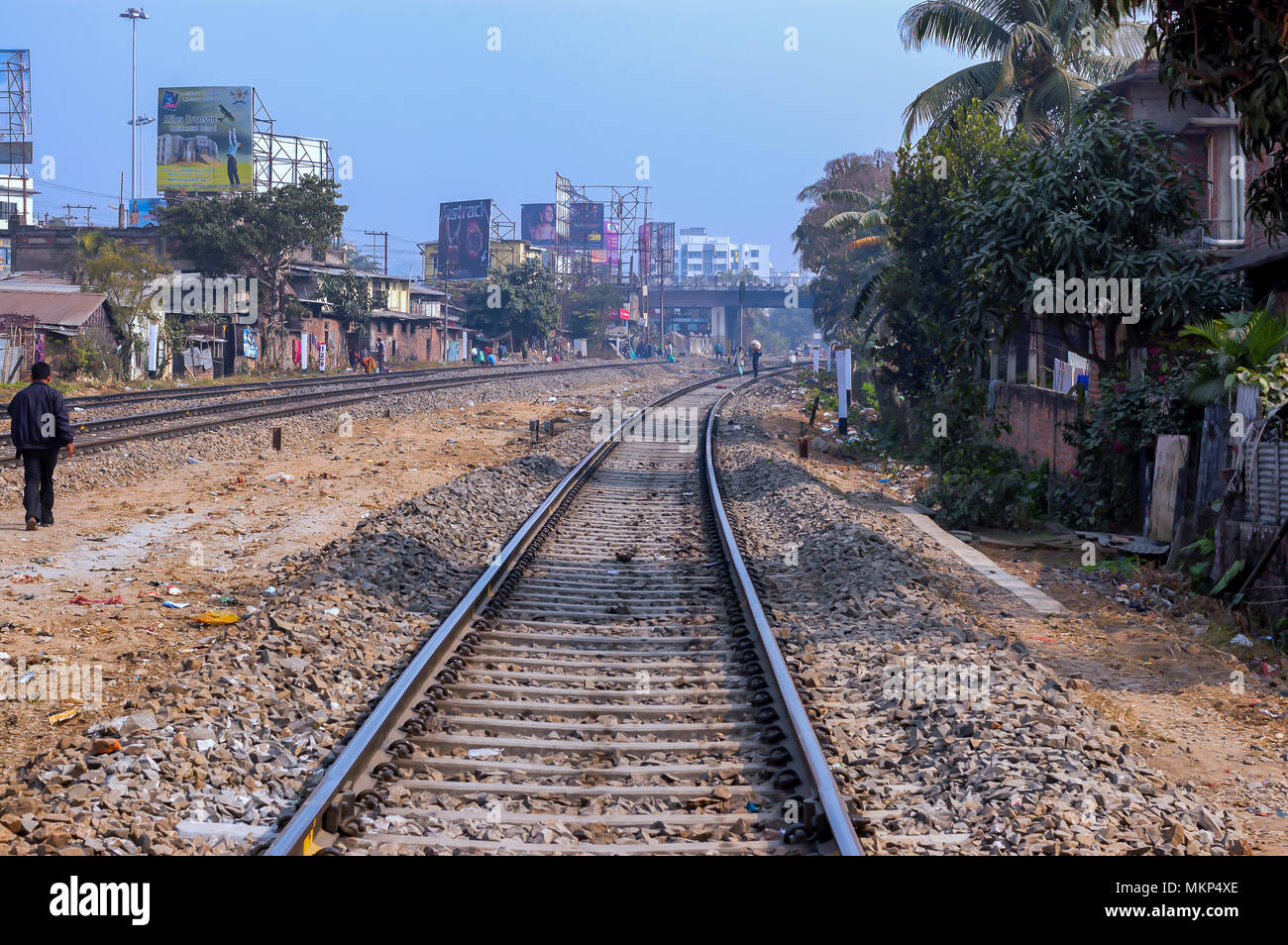 People walking nonchalantly on the sleepers of a railway tracks, in India. Residential houses and commercial establishments abuts the tracks. Stock Photo