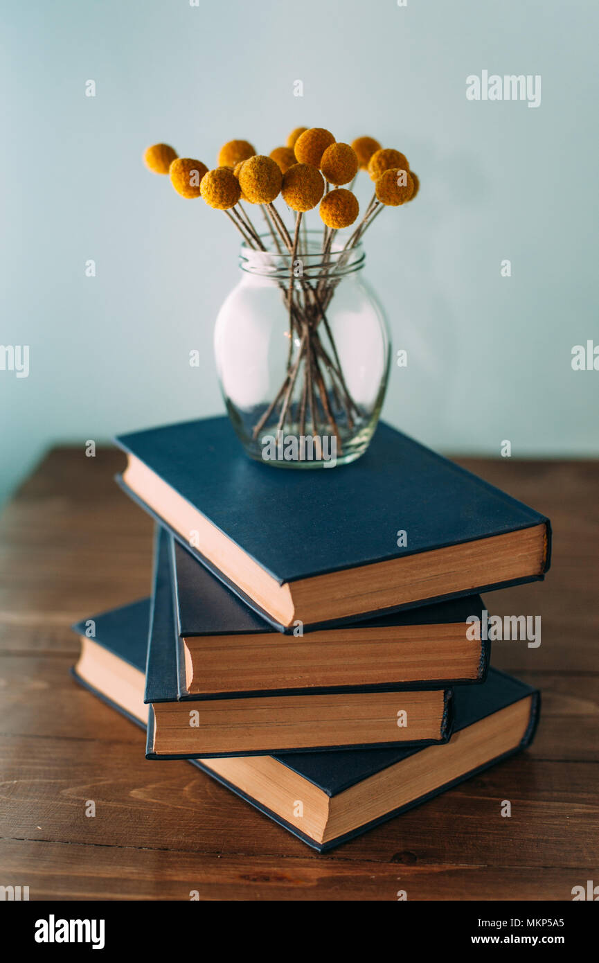 Stack of books and flowers Craspedia on wooden table Stock Photo