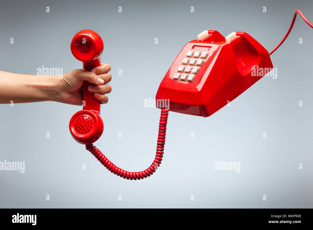 Hand holding telephone, classic red telephone receiver, old telephone isolated on white background flying in weightlessness. Stock Photo