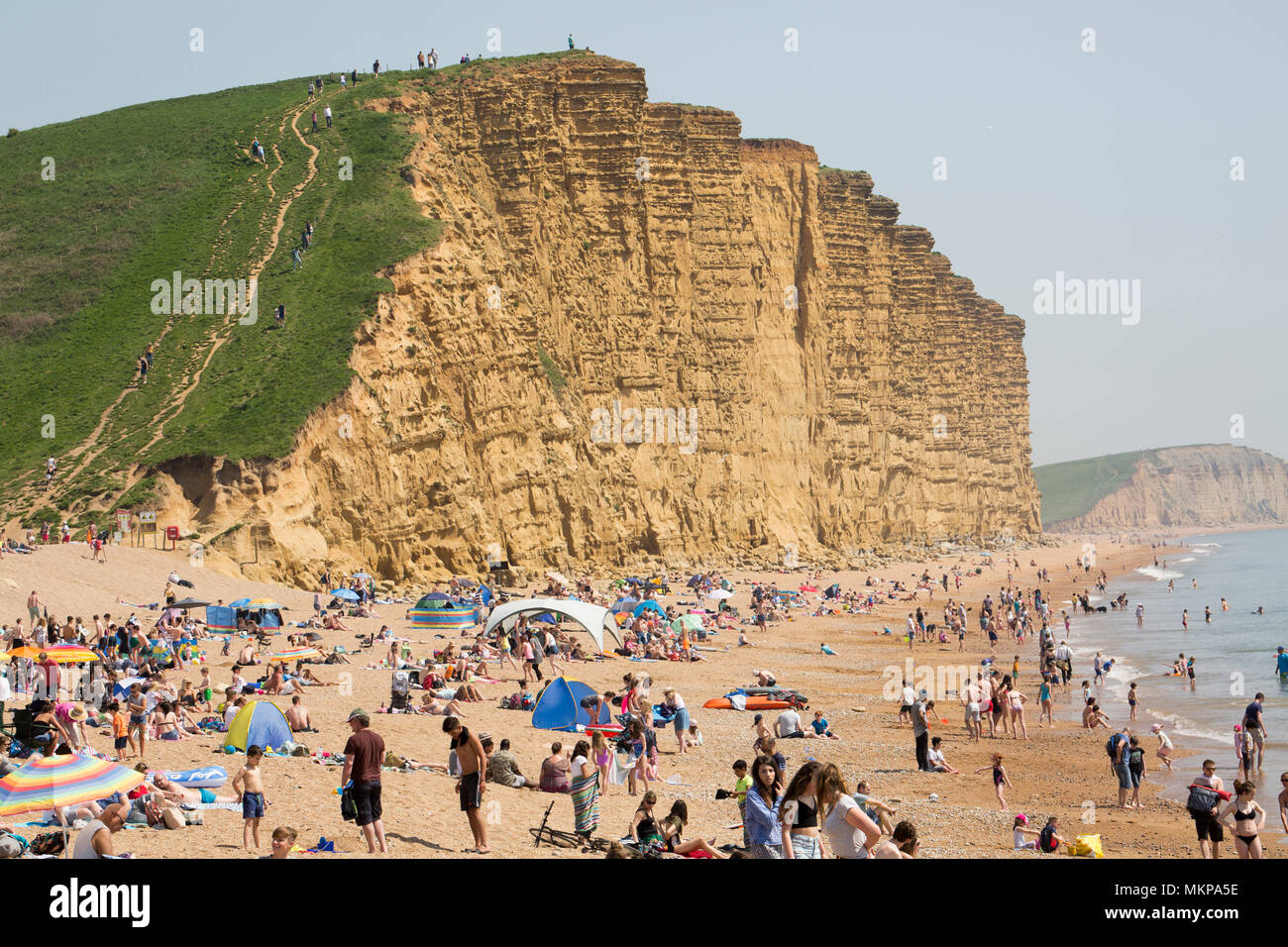 Visitors on East Cliff beach adjacent to West Bay and its harbour enjoy the sun and swimming on the hot May 7 Bank Holiday 2018. Stock Photo