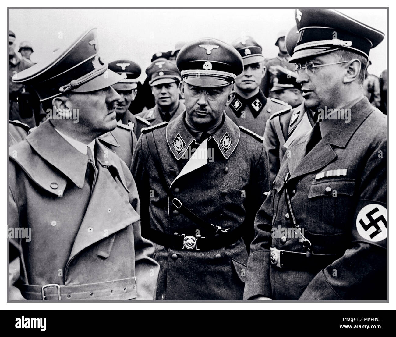 HITLER, HIMMLER, HENLEIN, Vintage WW2 1940's  B&W image of Adolf Hitler leader of the Nazi Party (Nationalsozialistische Deutsche Arbeiterpartei; NSDAP), Chancellor of Germany from 1933 to 1945 and Führer ('Leader') of Nazi Germany from 1934 to 1945  Heinrich Himmler Reichsführer of the Schutzstaffel (Protection Squadron; Waffen SS), and a leading member of the Nazi Party (NSDAP) of German & Konrad Henlein Reichsstatthalter and Gauleiter of the Reichsgau Sudetenland wearing a swastika armband. All in uniform standing talking, with SS officers grouped behind Stock Photo