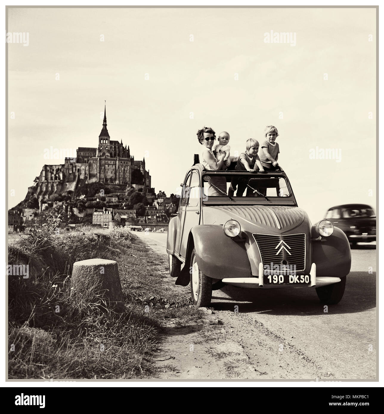 Vintage Citroën 2CV 1950 'deux chevaux'  typical notable family holiday vintage old historic French car press advertising with Le Mont Saint Michel behind Normandy France designed by Flaminio Bertoni: Stock Photo