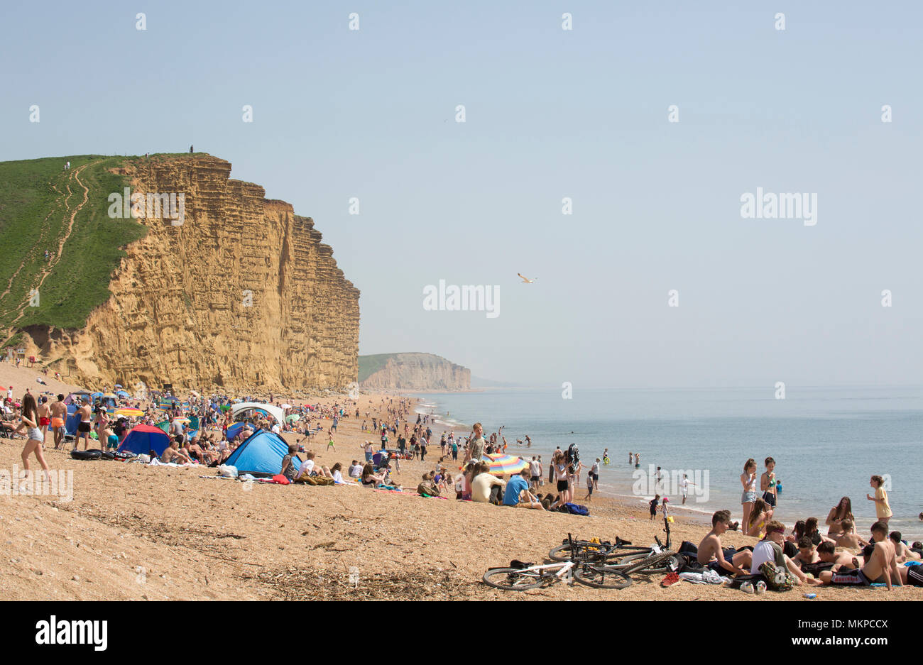 Visitors on East Cliff beach adjacent to West Bay and its harbour enjoy the sun and swimming on the hot May 7 Bank Holiday 2018. Stock Photo