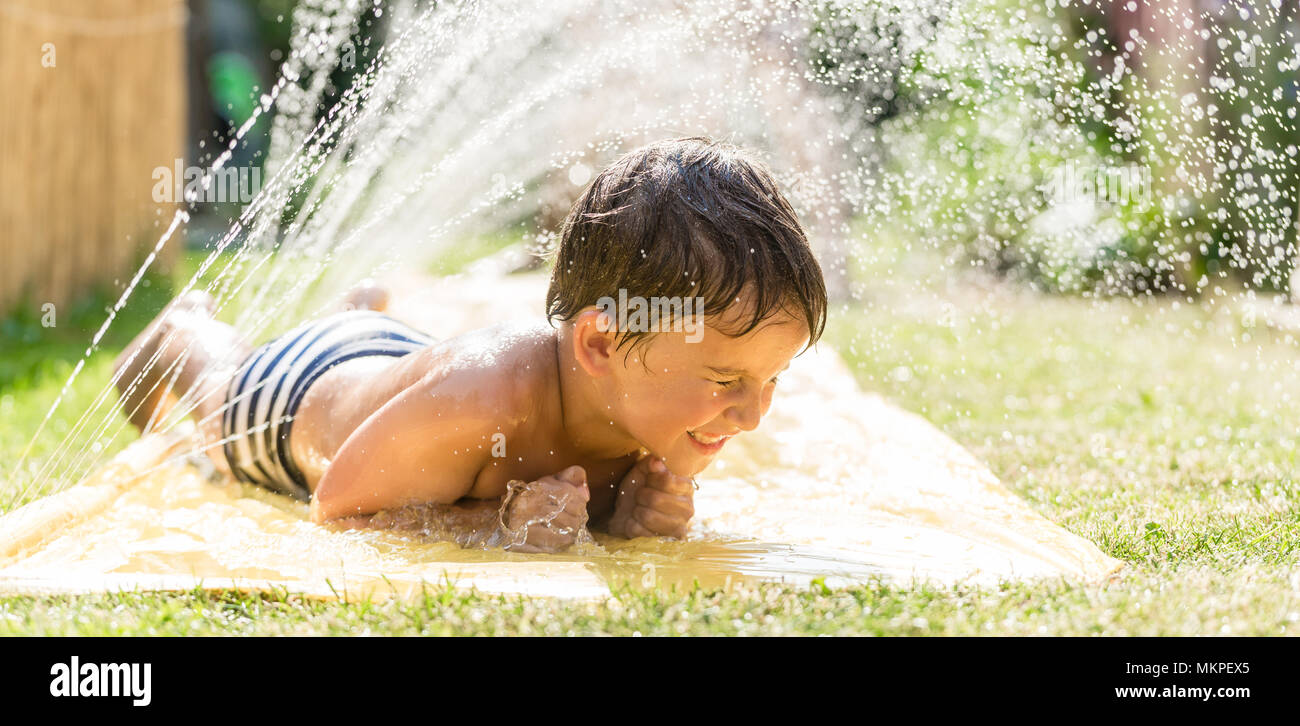 Boy cooling down with garden hose, family in the background Stock Photo