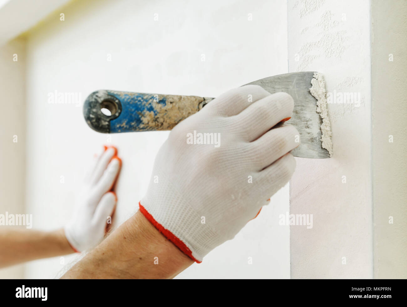 Decorative plaster coating. Man does ragged texture on the wall using a spatula. Stock Photo