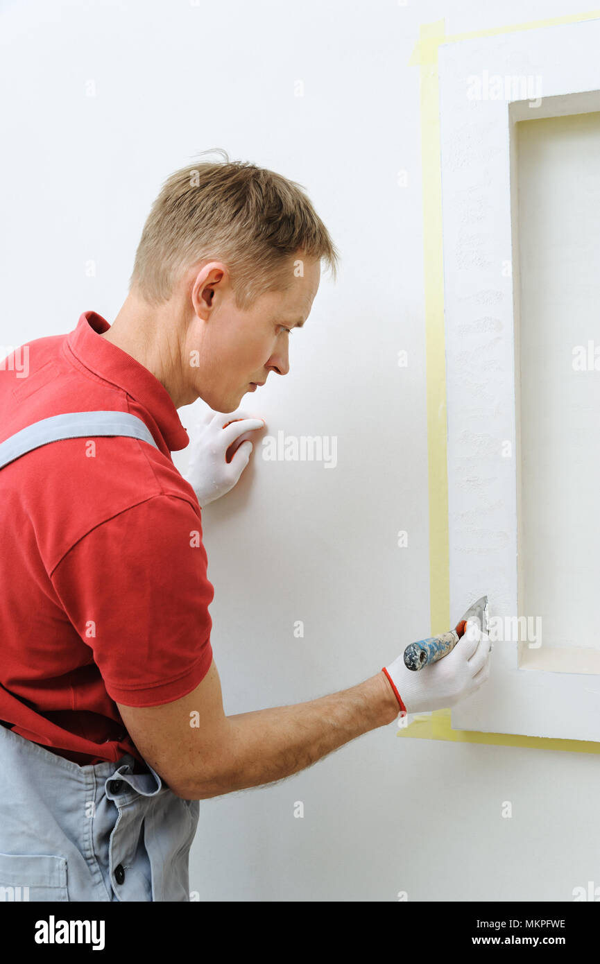 Decorative plaster coating. Man does ragged texture on the wall using a spatula. Stock Photo