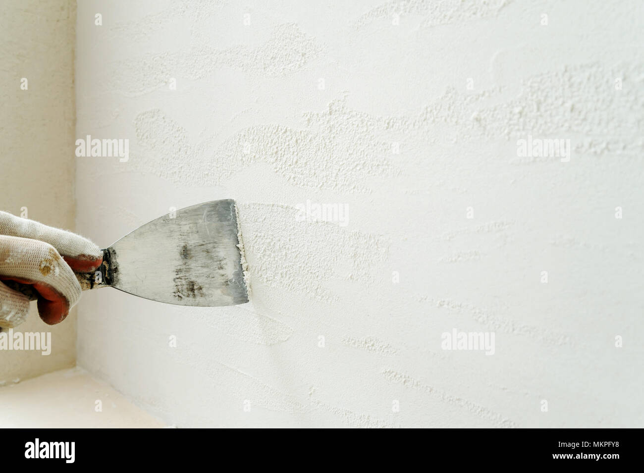 Decorative plaster coating. Man does ragged texture on the wall using a spatula. Stock Photo