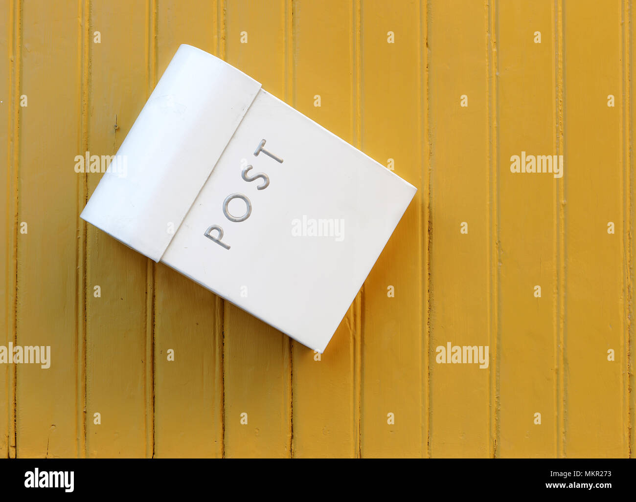 The white mailbox hanging awry on a yellow painted wooden wall. Stock Photo