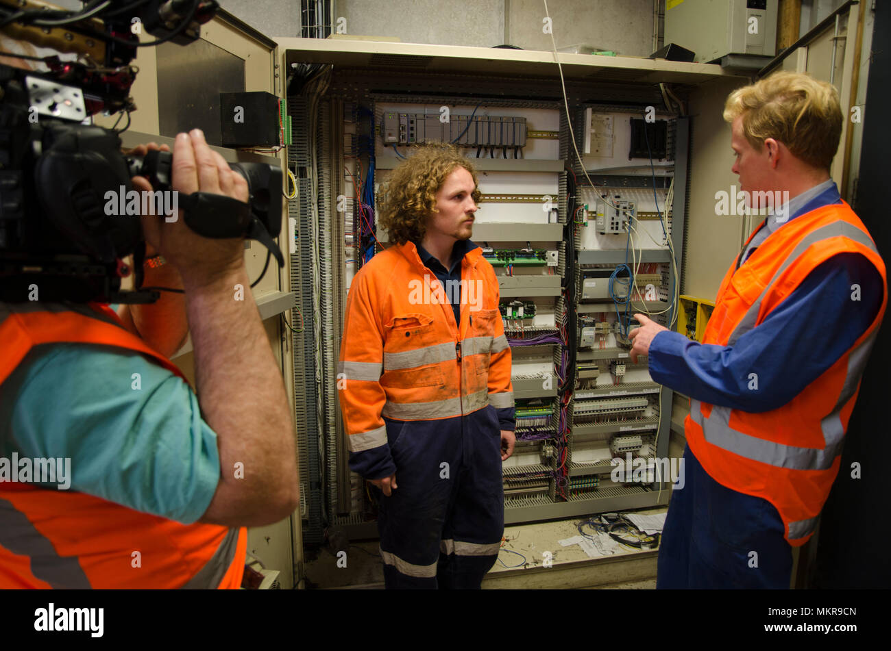 A cameraman films workers in the switchroom of a large factory Stock Photo