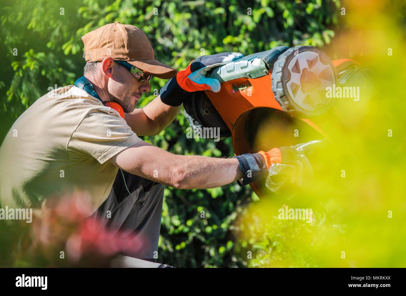 Caucasian Men Fixing Gasoline Lawn Mower in the Garden. Gardening Theme. Stock Photo