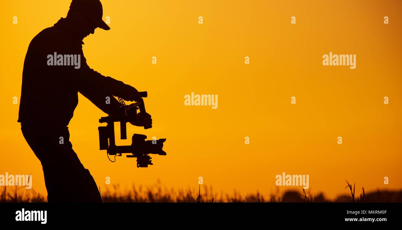 Video Stabilizer Operator. Taking Video Shoots Using DSLR Gimbal Equipment. Sunset Silhouette Concept. Stock Photo