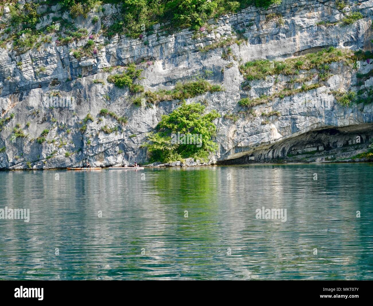 Kayakers paddling past the entrance to a recessed, cave-line area and rock striations at the edge of Lake Annecy, France Stock Photo