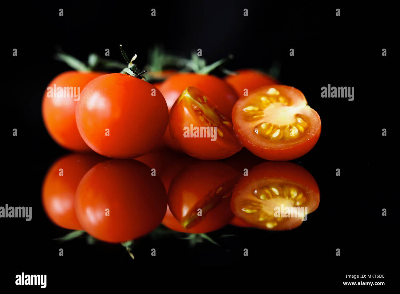 Reflected cherry tomatoes on the vine set against a black background Stock Photo