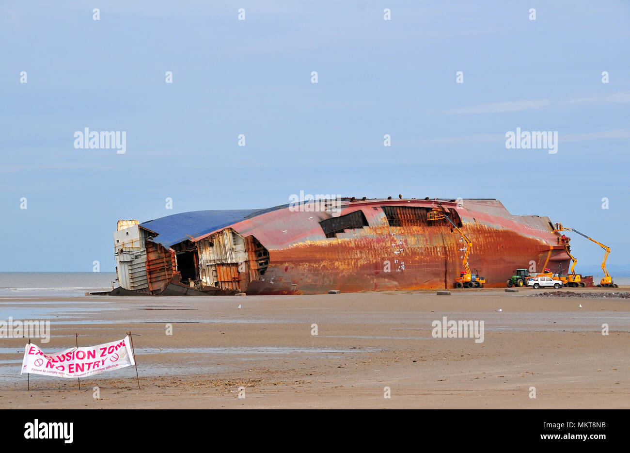 Blue grey sky view across low tide sand beach to Riverdance Ferry on its side and being dismantled with aerial platforms, Anchorsholme, Cleveleys, UK Stock Photo