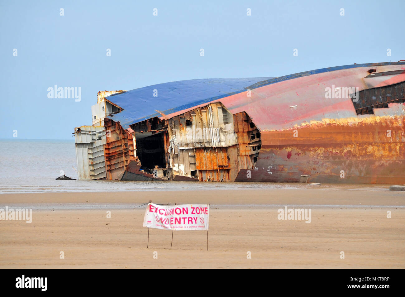 Grey sky receding tide view Riverdance Ferry wreck on its side, bow plates removed, with sand beach Exclusion Zone sign, Anchorsholme, Cleveleys, UK Stock Photo