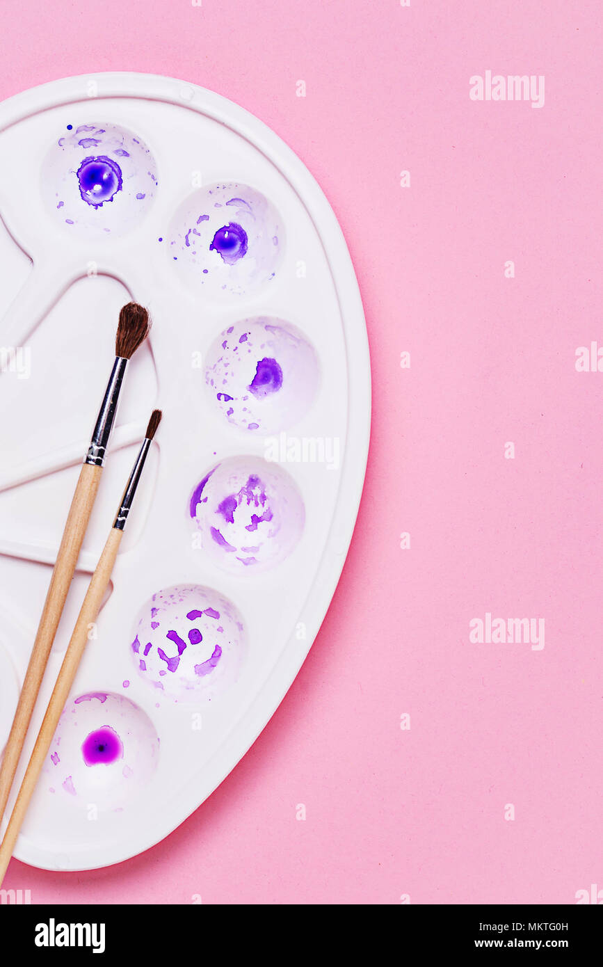 Artists palette with purple and violet paint and brushes on pink background Stock Photo