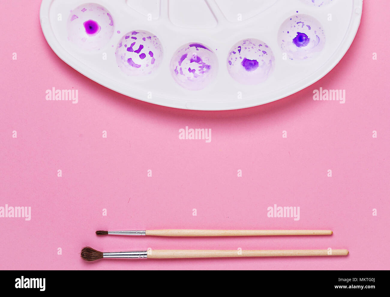 Artist€™s palette with purple and violet paint and brushes on pink background Stock Photo