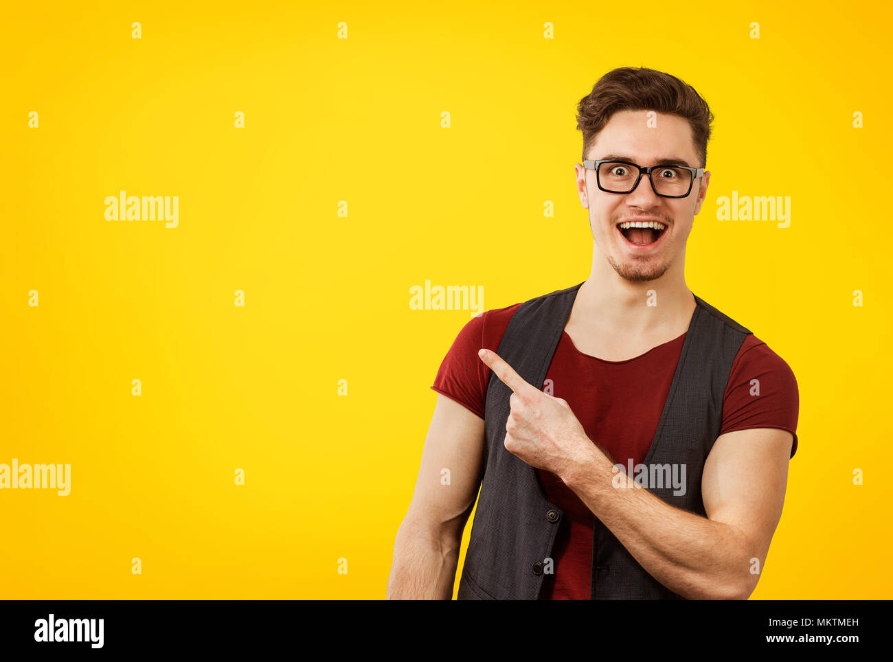Young stylish hipster man in glasses pointing happily away on orange yellow background Stock Photo