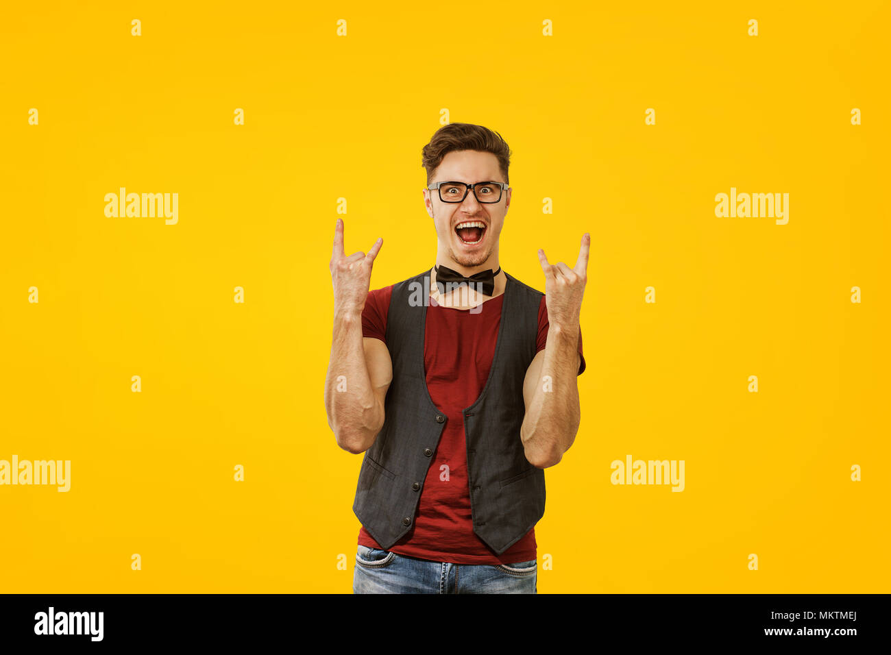 Portrait of young man in stylish cool outfit and glasses posing expressively on yellow background Stock Photo