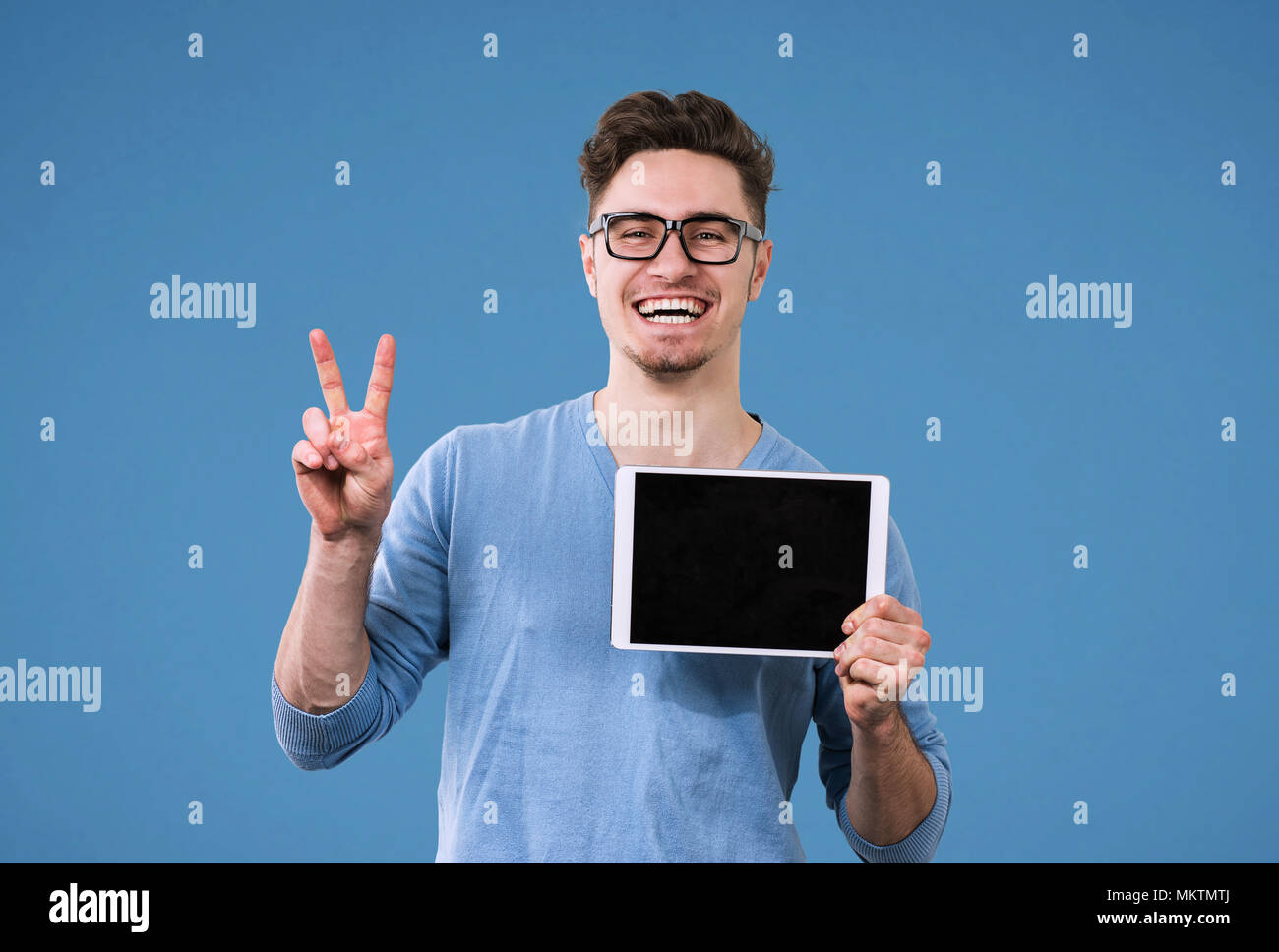 Happy hipster man in glasses with tablet computer giving victory sign Stock Photo