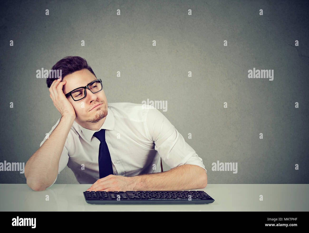 Young handsome man leaning on hand and falling asleep in boredom while working. Stock Photo
