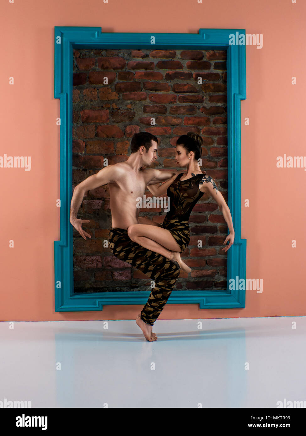 Modern ballet dancer couple in protective military color sport trousers and shirt performing art jump element with background Stock Photo