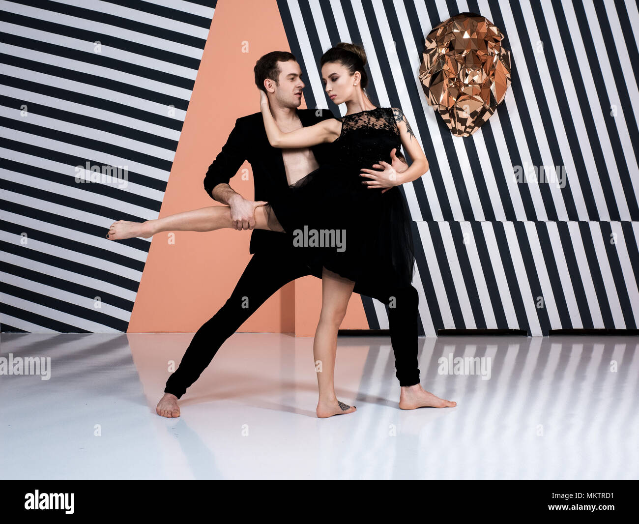 Modern ballet dancer couple in black jacket black trousers, black dress performing art jump element with zebra background Stock Photo