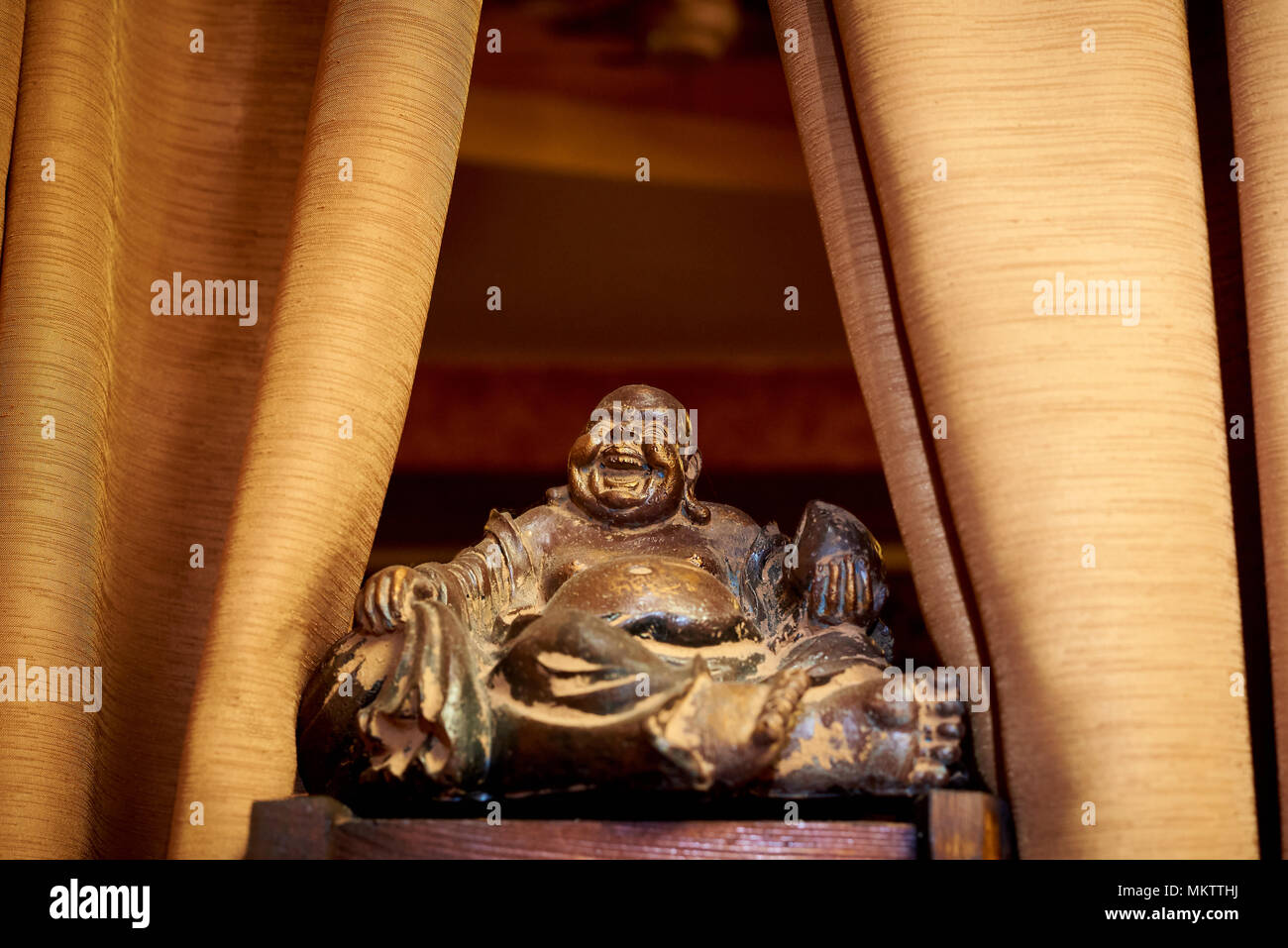 An old statuette close-up on a wooden surface on the sides of the curtain. Talisman Hotei by Feng Shui is the god of happiness, communication, fun and Stock Photo