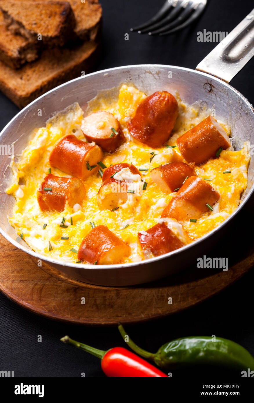 Breakfast of scrambled eggs and sausages in a pan on black background
