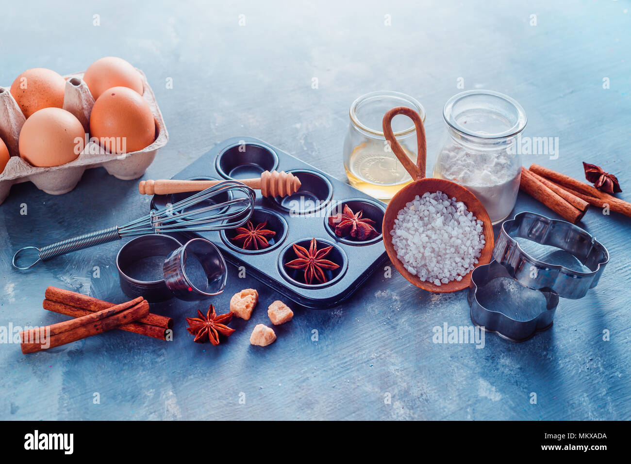 Baking utensils header. Muffin tin, sea salt, eggs, flour, oil and sugar with whisks and cookie cutters on a modern concrete background with copy spac Stock Photo