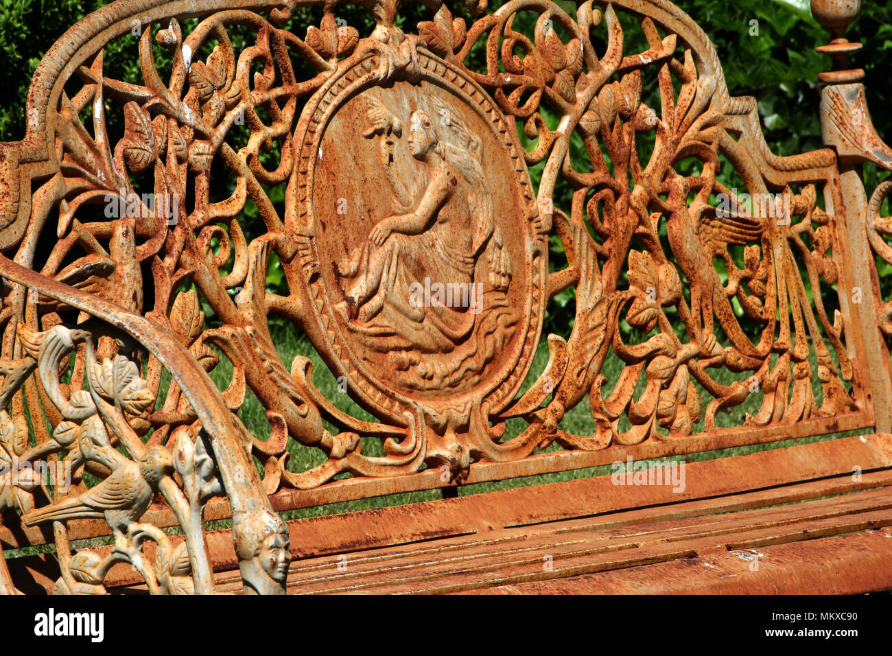 Heavily decorated metal bench, in outdoor space, covered in rust Stock