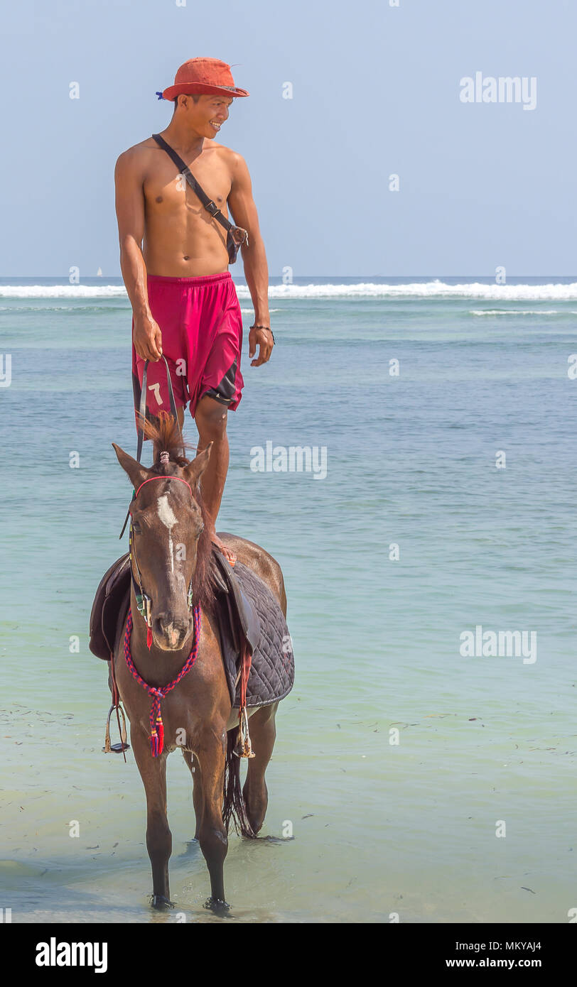 Beach with the blue and green ocean  behind and an Indonesian man standing on a horse, april 24, 2018, Gili Trawangan, Indonesia Stock Photo