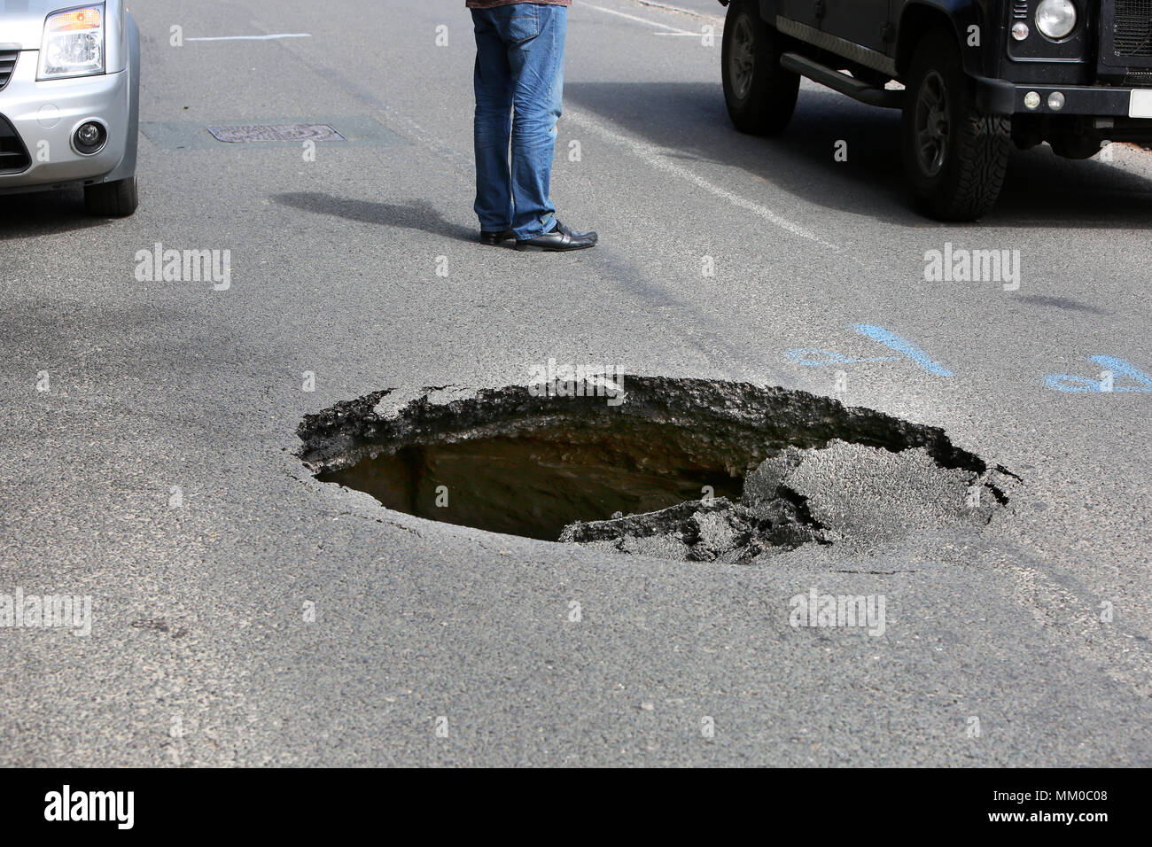 Midhurst, Near Chichester, West Sussex, UK. A huge sink hole pictured on Bepton Road, close to the high street and causing long delays. Members of the public directed traffic for over 45minutes until police arrived to close the road.  Wednesday 9th May 2018 © Sam Stephenson/Alamy Live News. Stock Photo