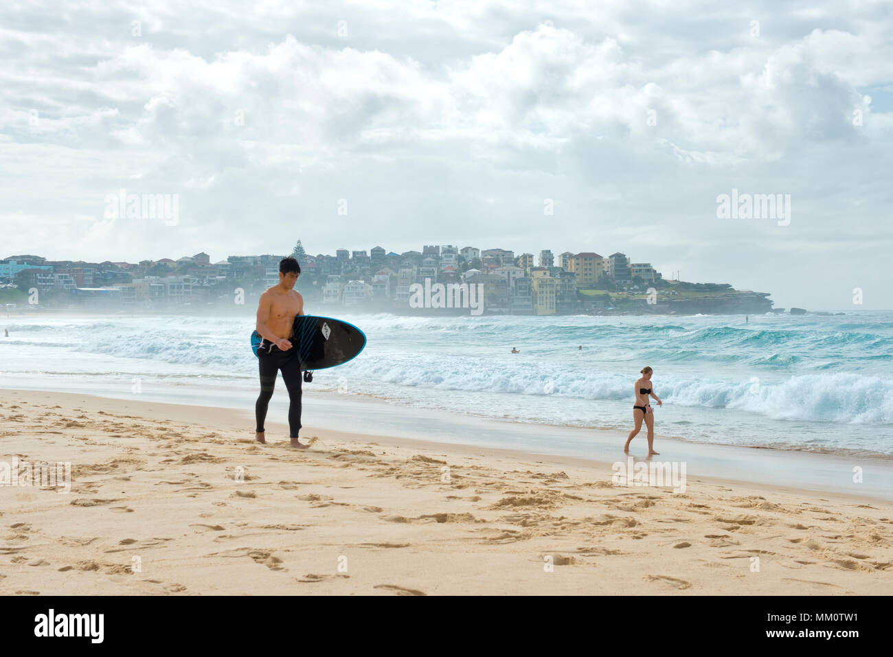 Surfer with board and woman in bikini strolling on Bondi beach Stock Photo