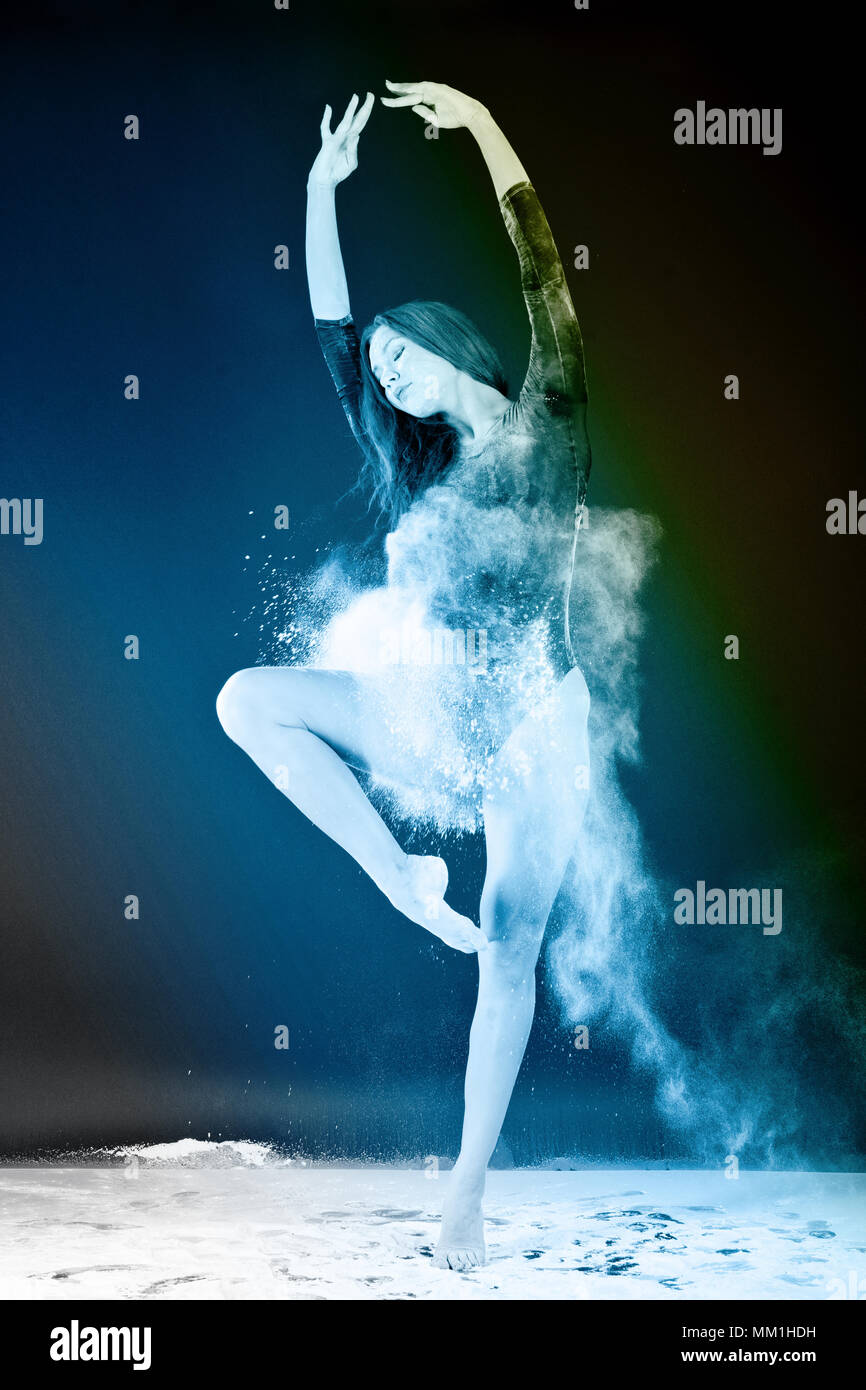 Slender girl dancing in white dust, Studio shot. Illuminated with colored lanterns. Blue and mustard on black background Stock Photo